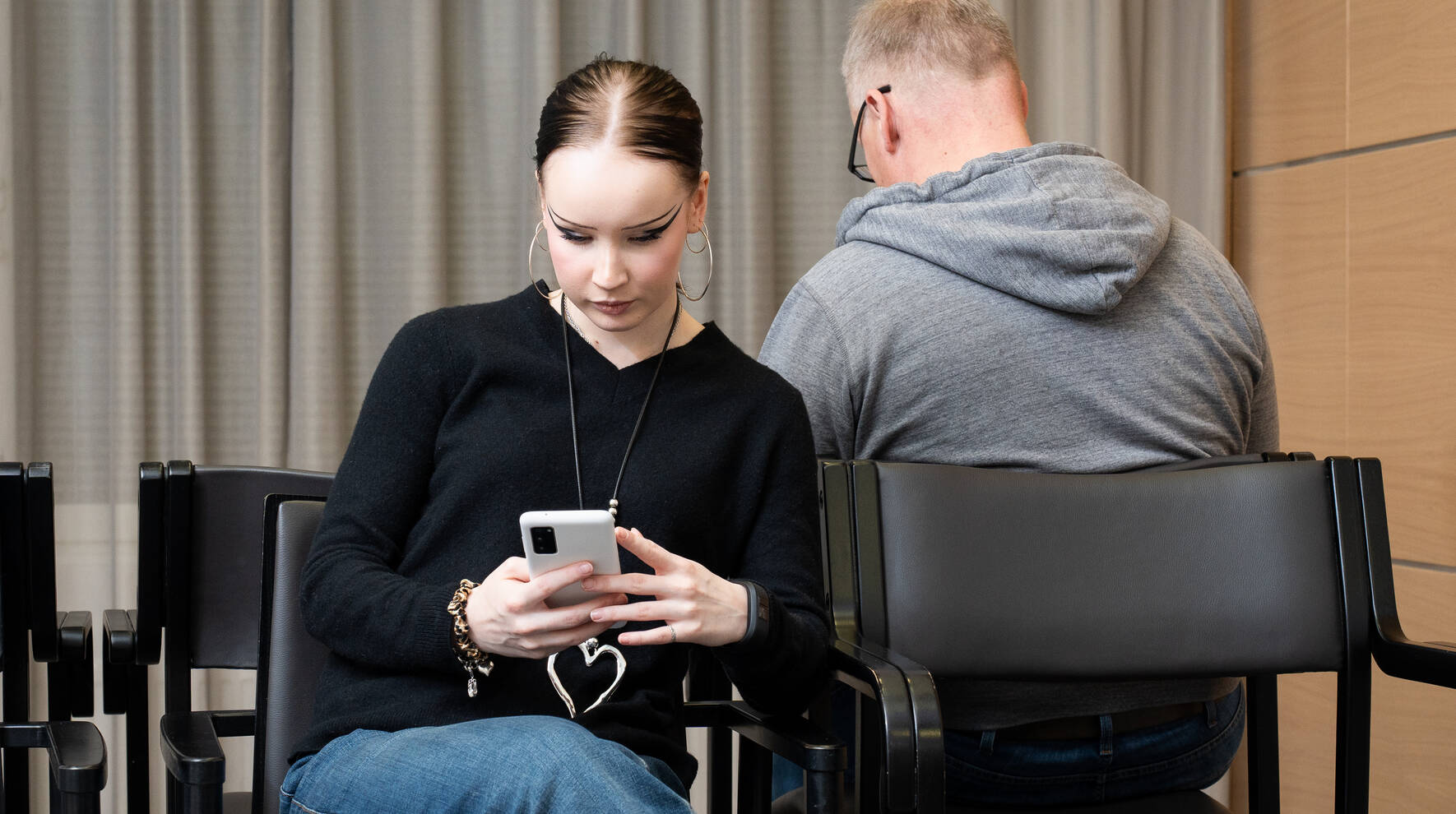 Nuori nainen istuu vastaanottohuoneessa ja katsoo puhelinta.