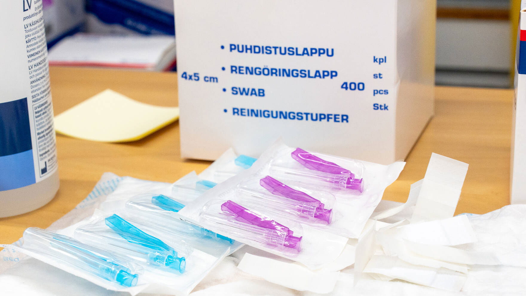 Violetteja ja sinisiä rokotusneuloja muovipakkauksissa pöydällä.