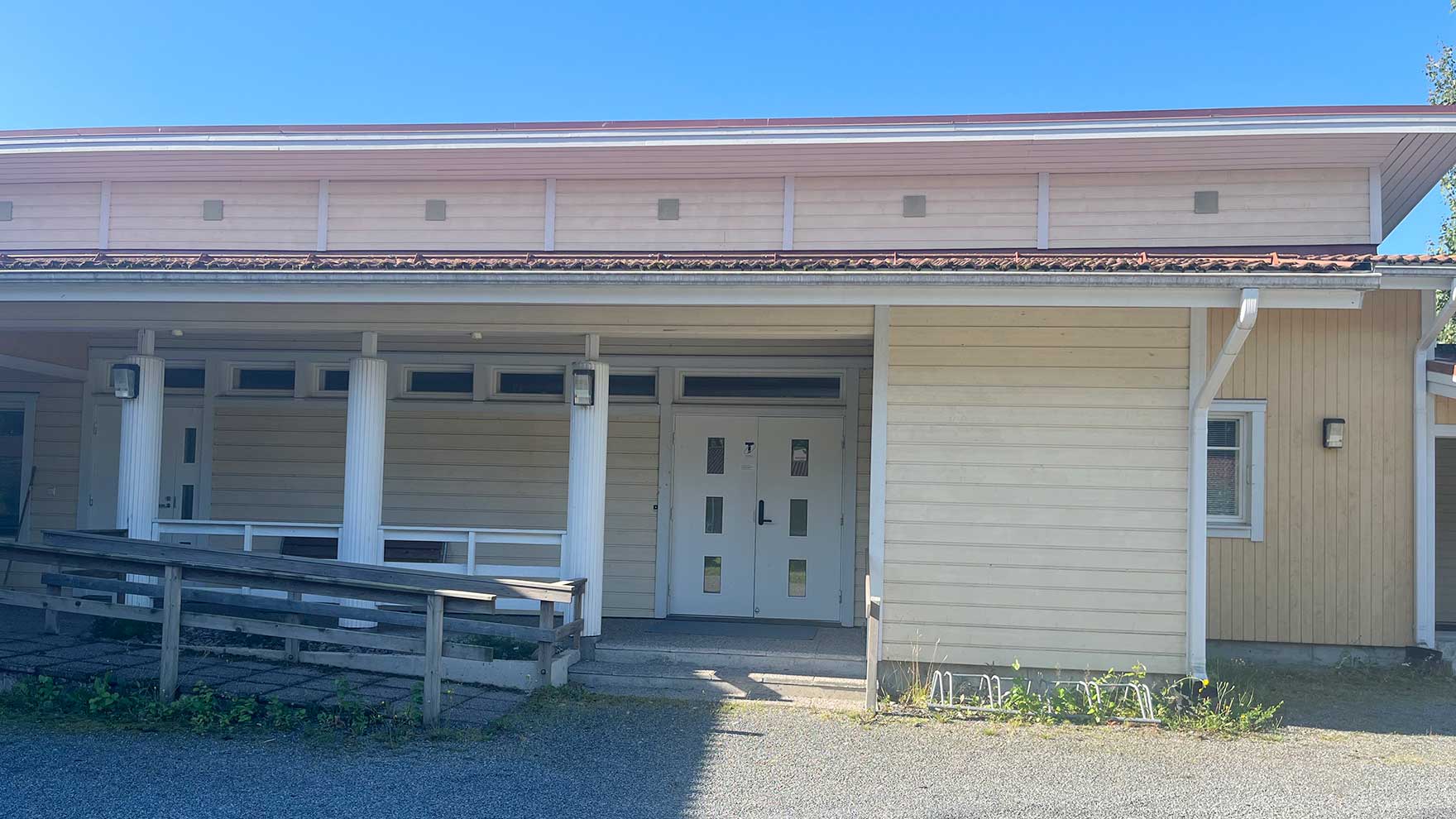 Vaalen matalan puurakennuksen sisäänkäynti, jonka edessä puinen kulkuväylä pyörätuolille.