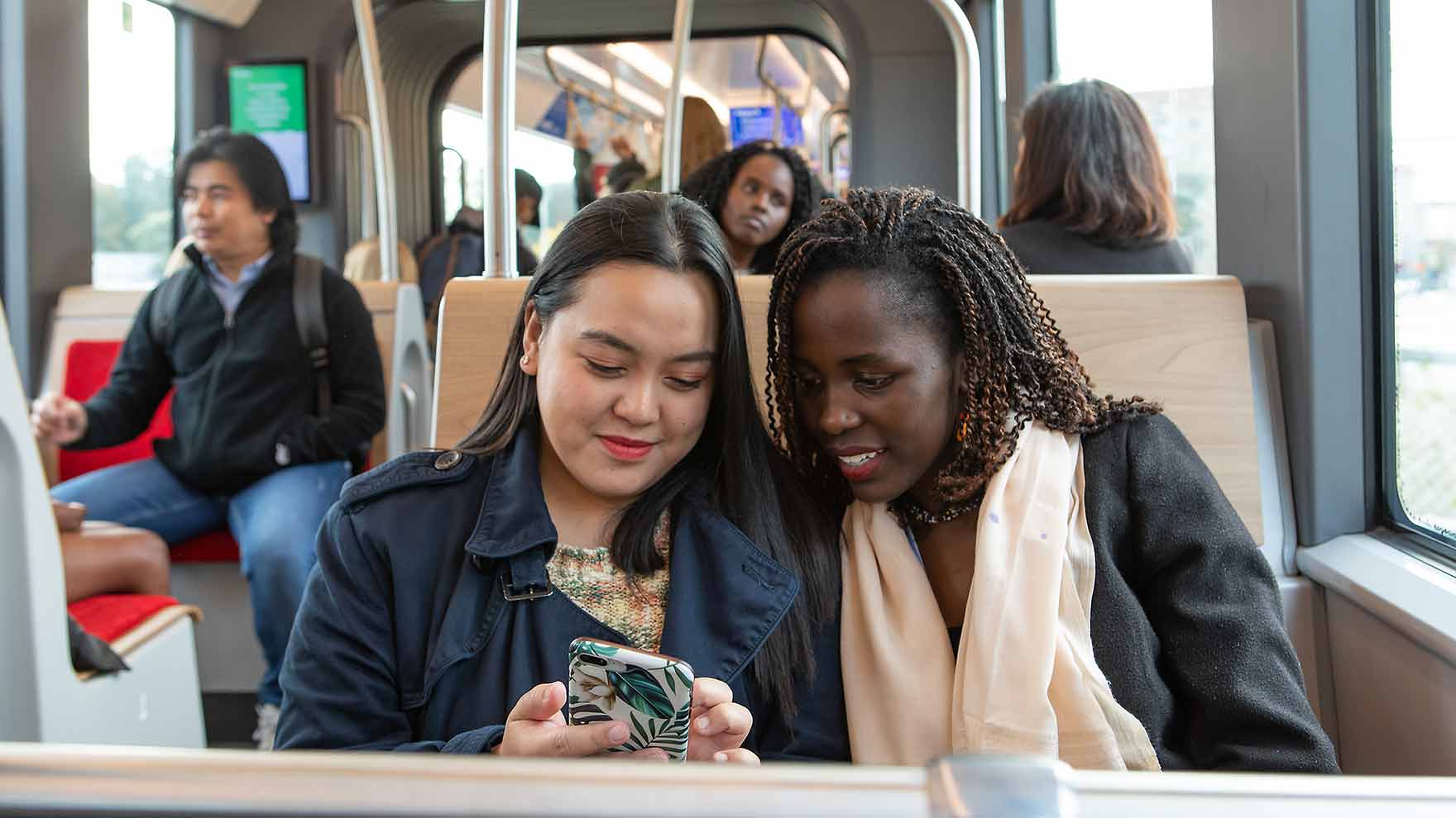 Kaksi naista istuu vierekkäin ratikassa ja katsoo yhdessä toisen kännykkää.