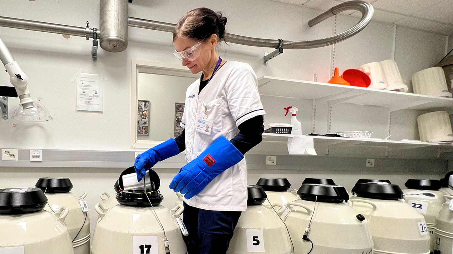 Hedelmöityshoitobiologi Tiina Mikkilä avaa nestetyppisäiliön kantta. Säiliöitä on lattialla useita.