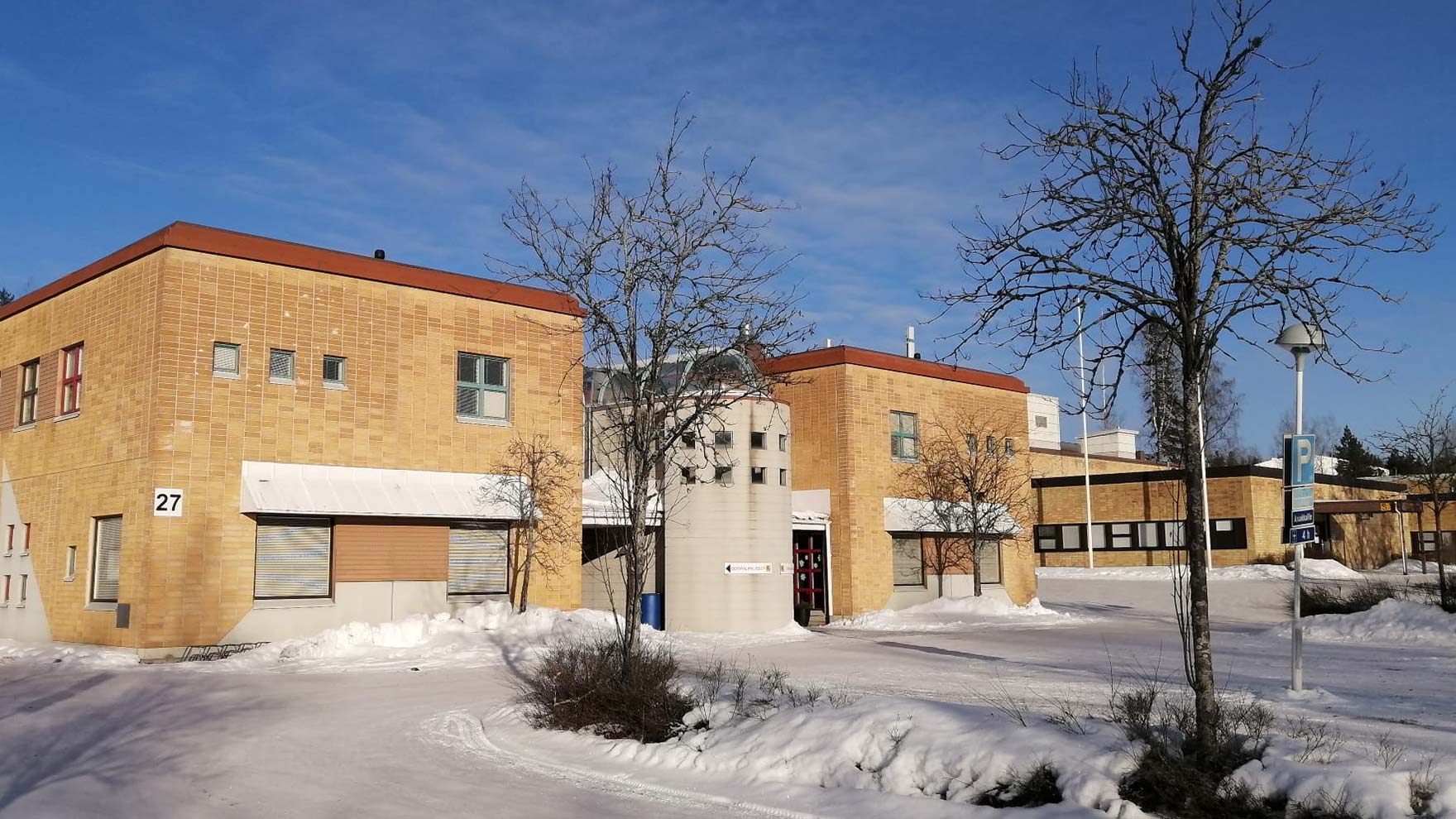 Vaalenruskea tiilirakennus, jonka pihalla on lunta.