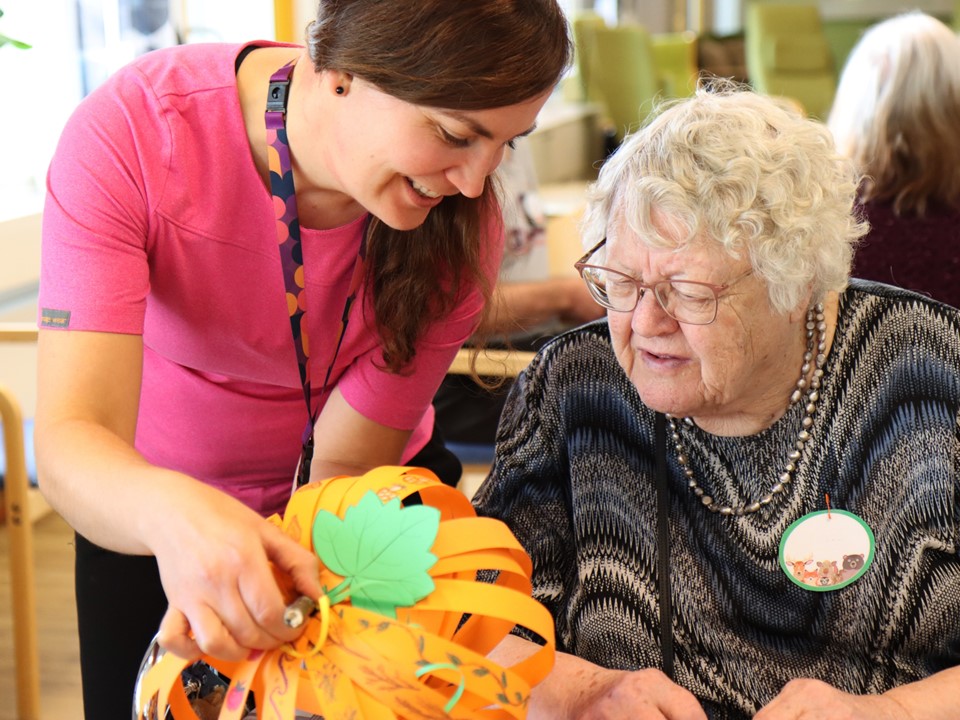 Pirkanmaan hyvinvointialueen työntekijä katsoo ikäihmisen kanssa paperista, askarreltua kurpitsaa.