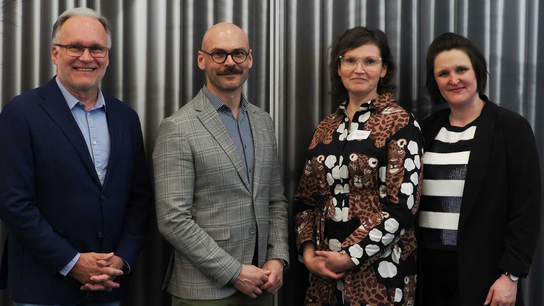 Kaksi miestä vasemmalla ja kaksi naista oikealla poseeraa kameralle.