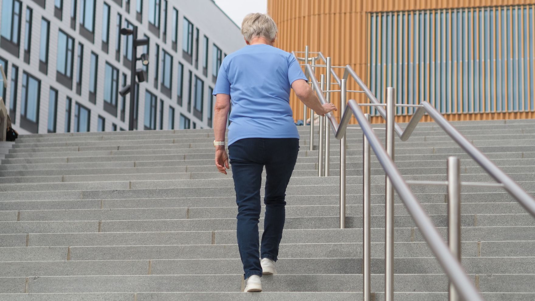 Nainen nousee ulkotiloissa kiviportaita ylös päin kaiteesta kiinni pitäen.