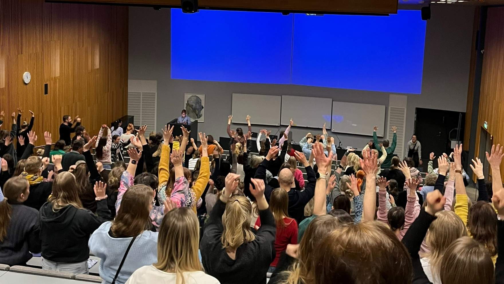 Yleisö venyttelee käsiään kattoa kohti seminaarin taukojumpassa.