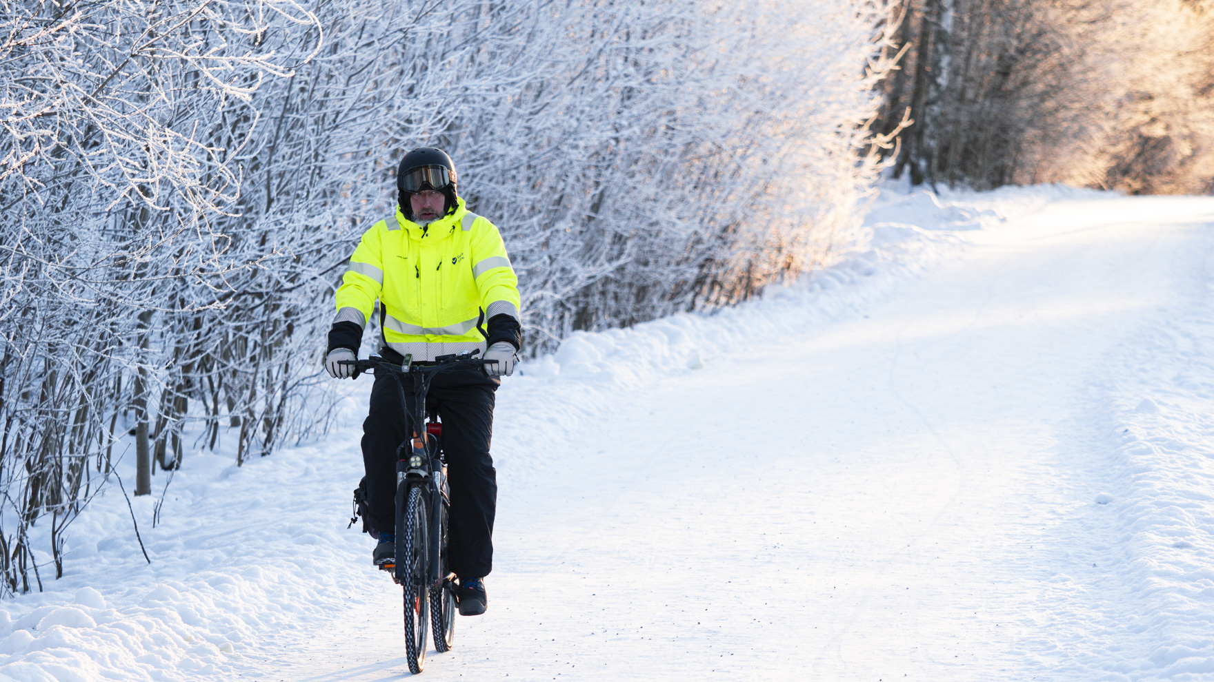 Mies polkee sähköpyörällä lumen peittämällä kevyenliikenteen väylällä.