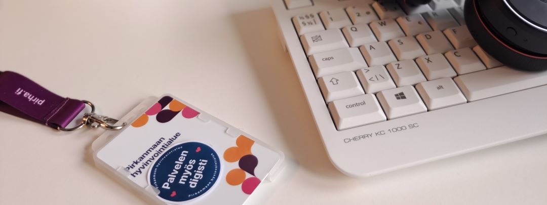 Henkilökuntakortti, jossa lukee palvelen myös digisti. Oikealla näkyy osa näppäimistöstä ja kuulokkeista.